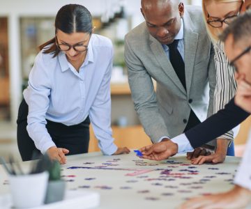 Diverse group of smiling businesspeople standing together around an office table trying to solve a jigsaw puzzle